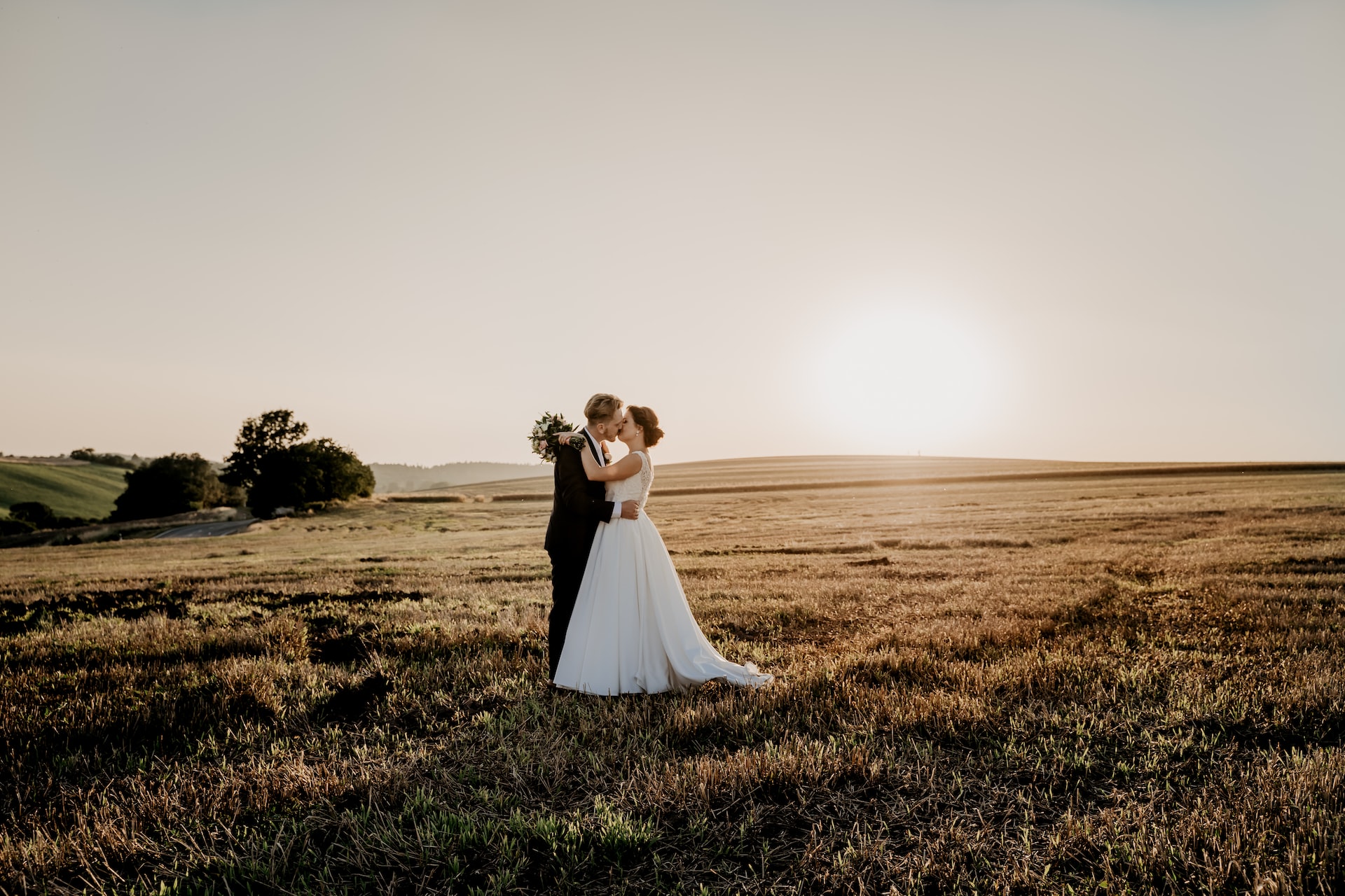 Bride and groom couple standing in a field at sunset