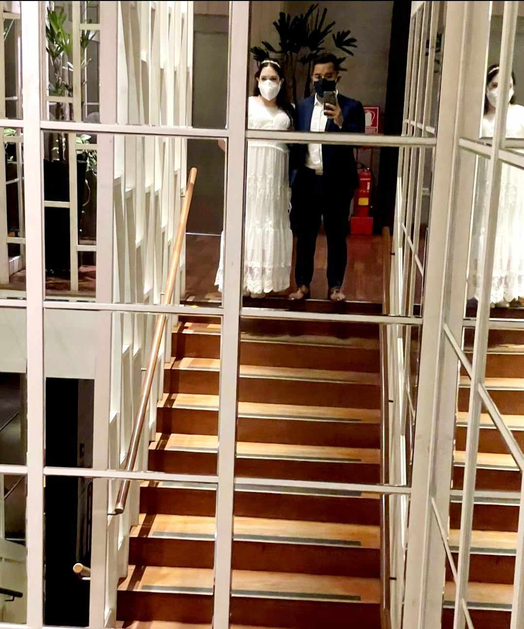 Bride and groom stand on the stairs in front of a mirror.