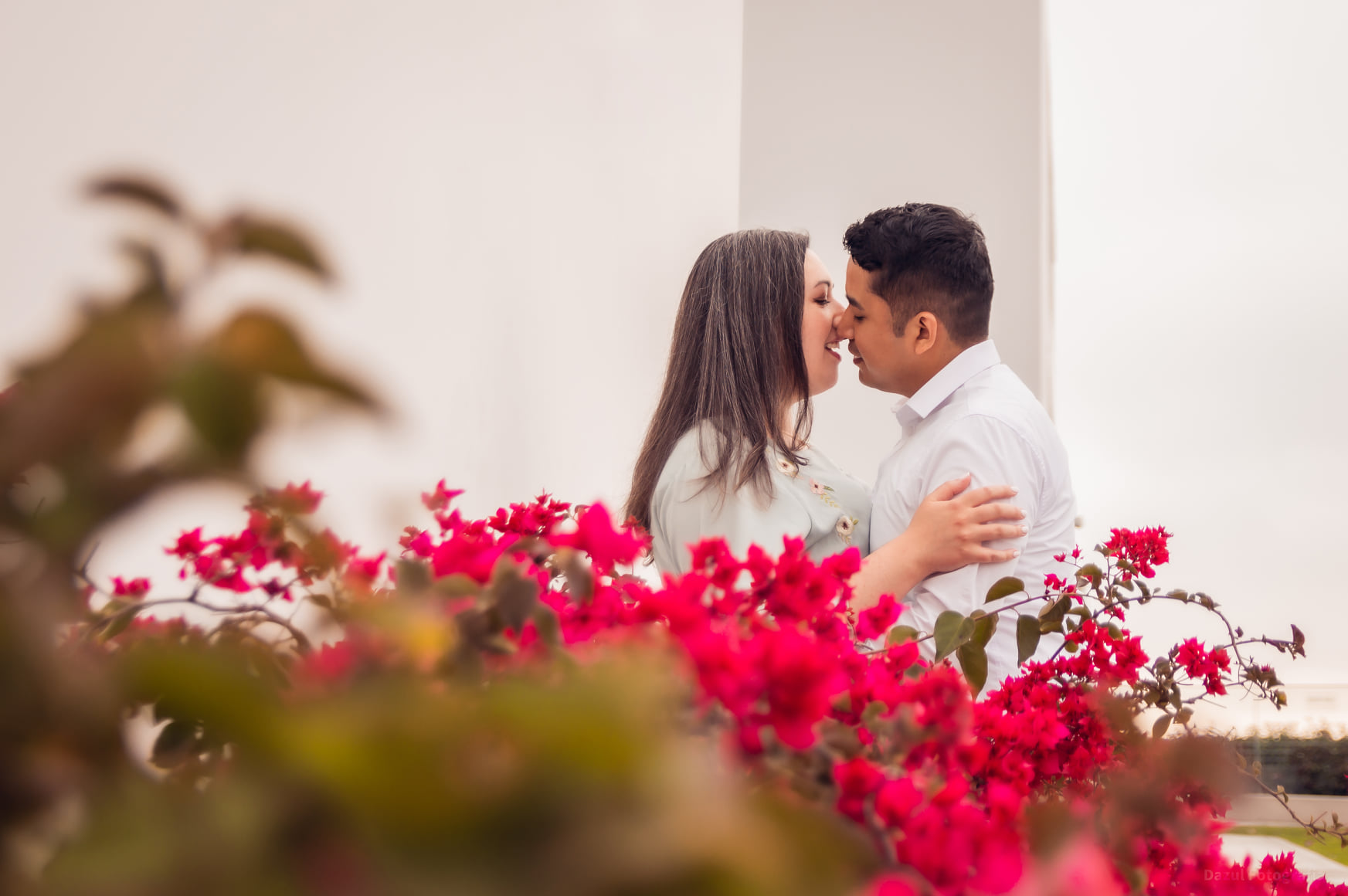Man and woman about to kiss behind fuchsia flowers.