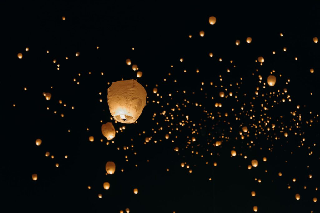 Paper lanterns floating on black sky at night.