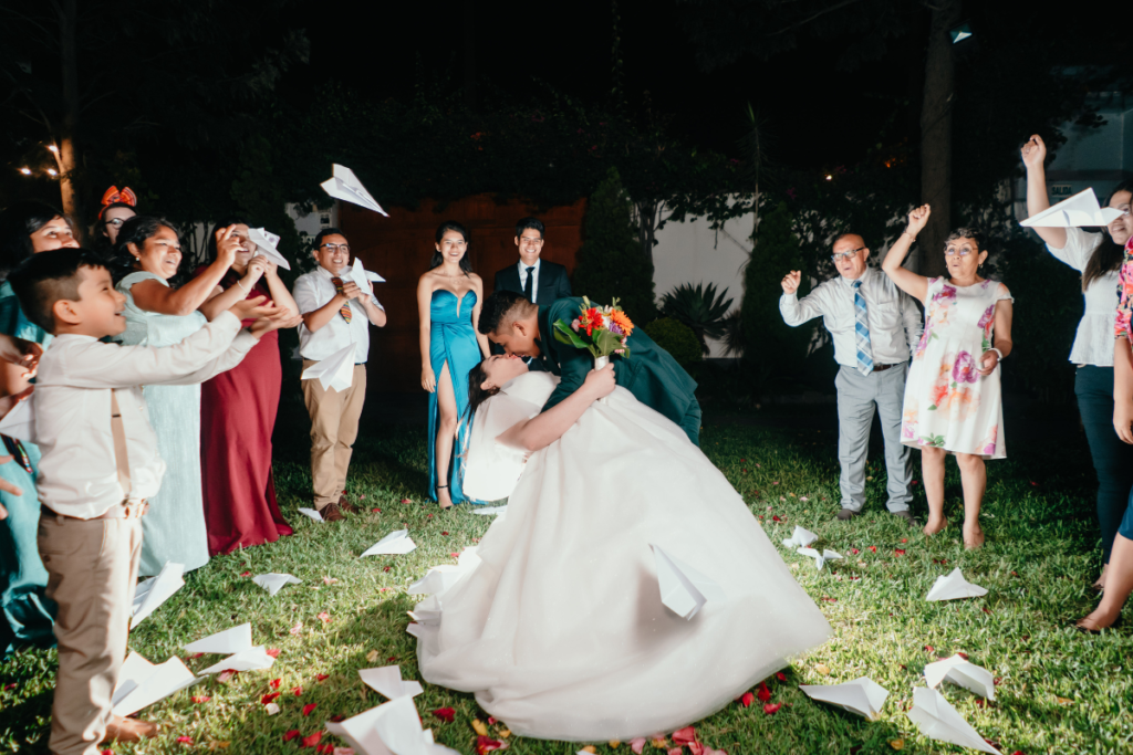 Bride and groom kiss during a paper airplane wedding send-off at night.